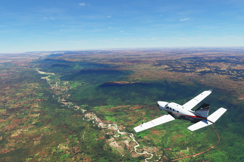 Socata TBM flying over river and high cliffs.